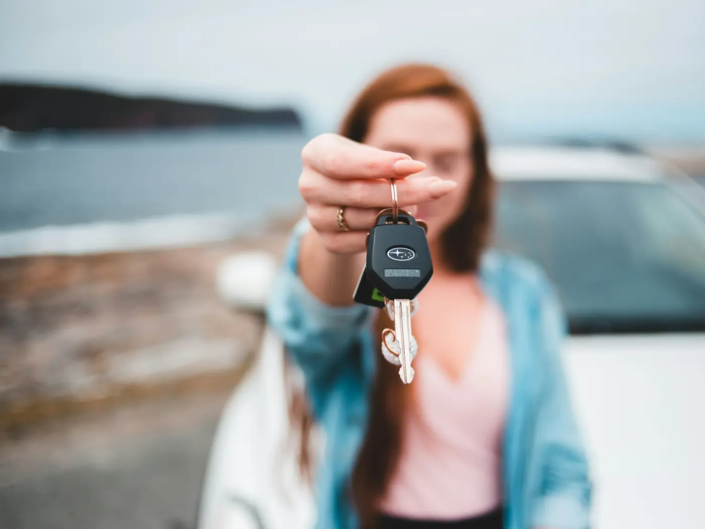 Woman holding out a car key in front of a white car