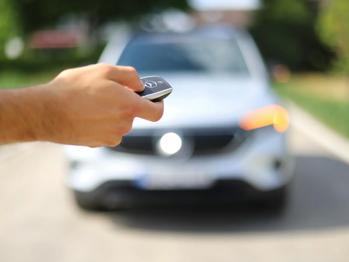 Hand pointing a key fob at a car to unlock it