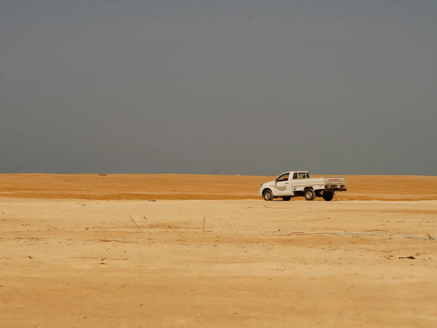 White pickup truck driving across a flat desert under a grey sky
